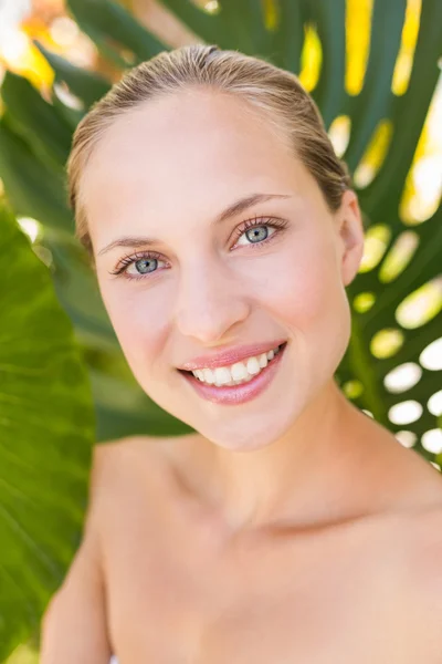 Beautiful blonde smiling at camera behind leaf — Stockfoto