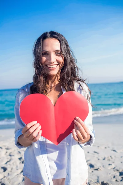 Mujer sonriente sosteniendo tarjeta de corazón en la playa — Foto de Stock