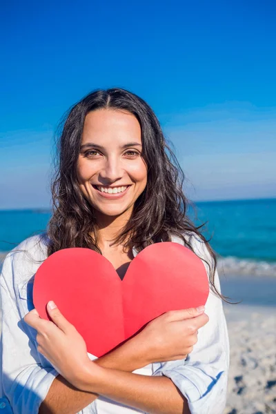 Smiling woman holding heart card at the beach — ストック写真