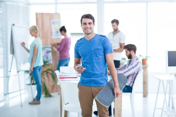 Empresario de pie con su monopatín sonriendo a la cámara — Foto de Stock