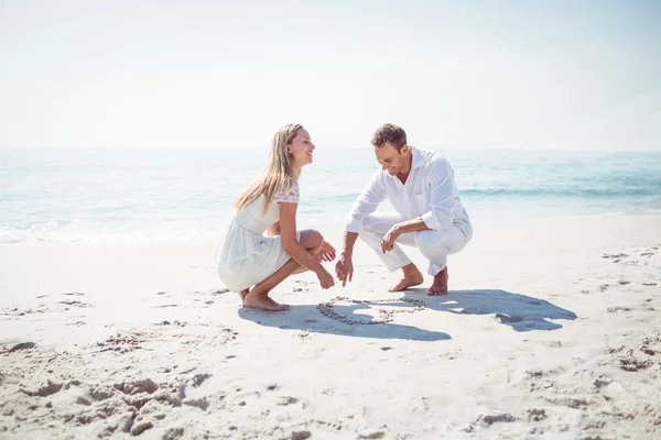 Casal feliz desenhando forma de coração na areia — Fotografia de Stock