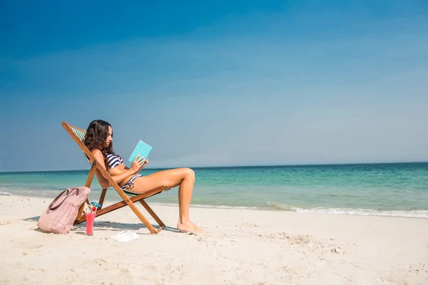 Morena bonita lendo um livro na cadeira de praia — Fotografia de Stock