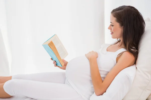 Smiling pregnancy reading in bed — 스톡 사진