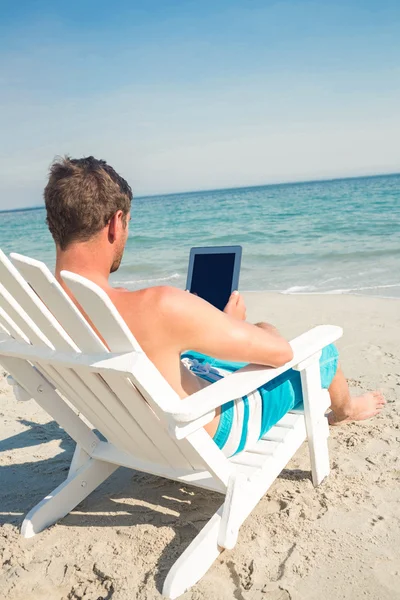 Man using digital tablet on deck chair at the beach — Zdjęcie stockowe