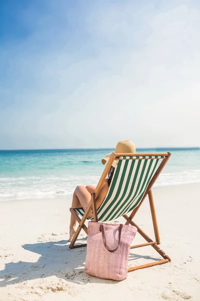Rear view of pretty brunette relaxing on deck chair at the beach — Stok fotoğraf