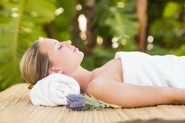 Loira no tapete de bambu com flores no spa — Fotografia de Stock