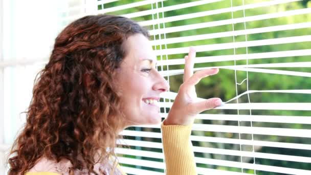 Mujer mirando a través de persiana enrollable — Vídeos de Stock