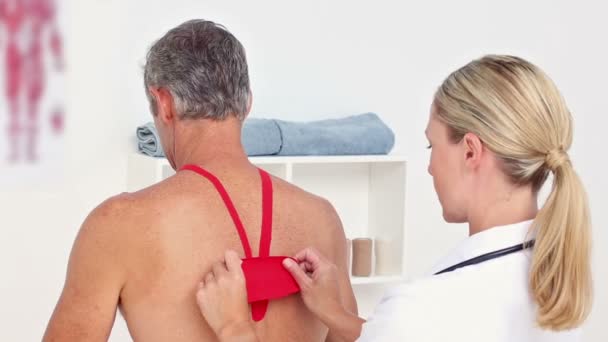 Médico aplicando cinta de kinesio en su espalda pacientes — Vídeos de Stock