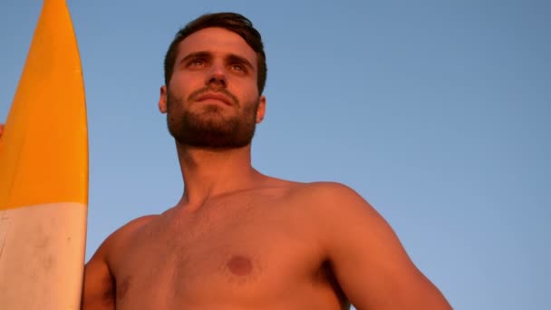 Hombre con una tabla de surf mirando hacia otro lado — Vídeos de Stock