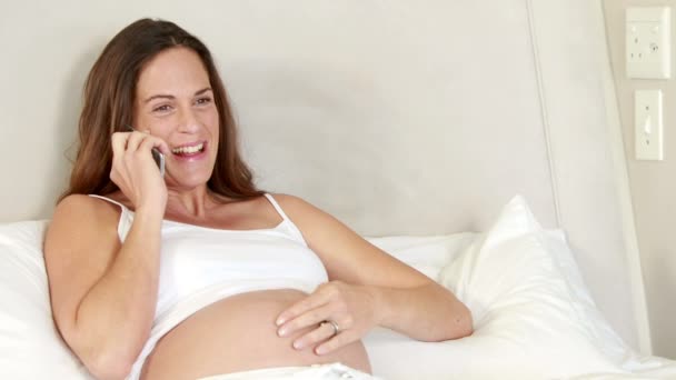 妊娠中の女性がベッドの上で携帯電話で話しています。 — ストック動画