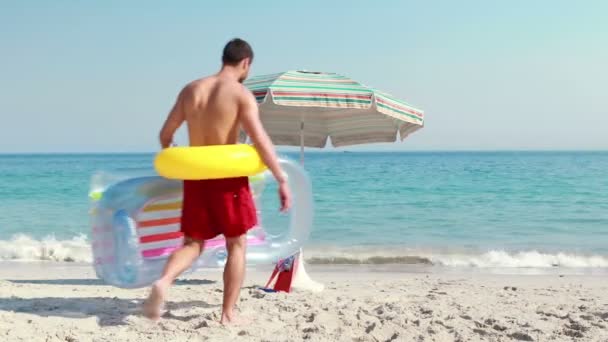 Мужчина лежит на пляже с резиновым кольцом — стоковое видео