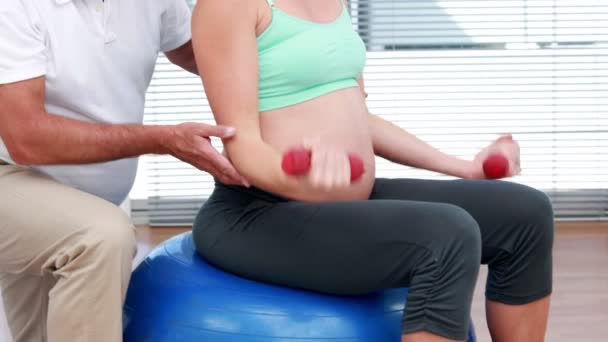 Pregnant woman lifting dumbbells on an exercise ball — Stock Video