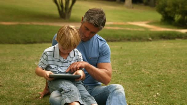 Ο πατέρας με το γιο του χρησιμοποιώντας το δισκίο στο πάρκο — Αρχείο Βίντεο
