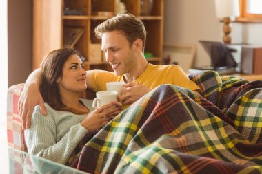 couple cuddling on couch under blanket clipart