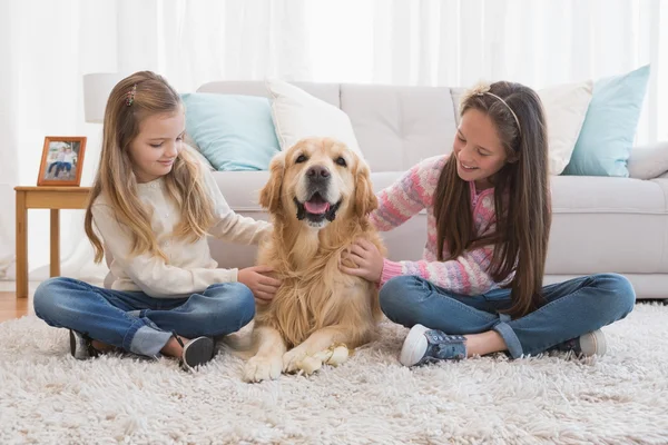 Sisters petting golden retriever on rug — Stock Photo, Image