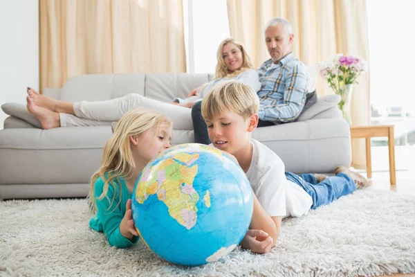 Siblings looking at globe on floor — Stock Photo, Image