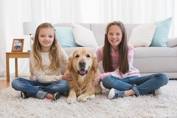 Schwestern streicheln Golden Retriever auf Teppich — Stockfoto