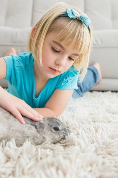 Ragazza sdraiata sul tappeto accarezzando coniglio — Foto Stock