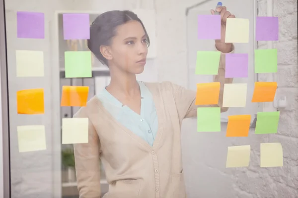 Businesswoman writing on sticky notes on window — Stock Photo, Image