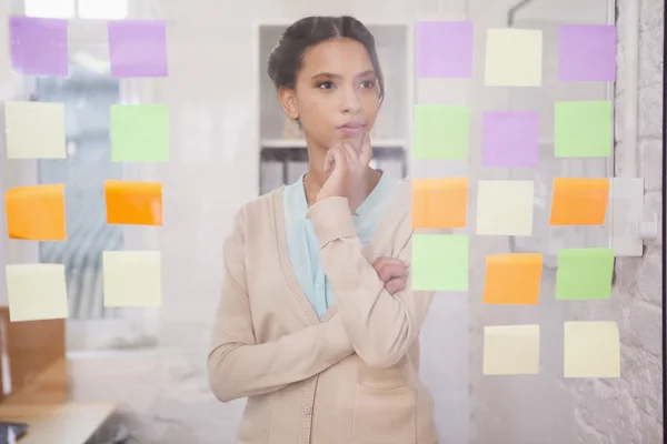 Businesswoman looking at sticky notes on window — Stock Photo, Image