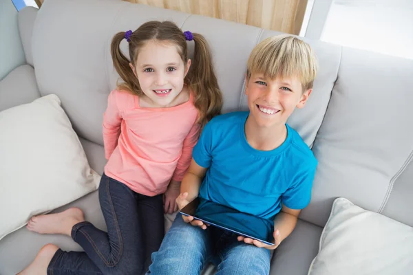 Happy siblings using tablet pc on sofa — Stock Photo, Image