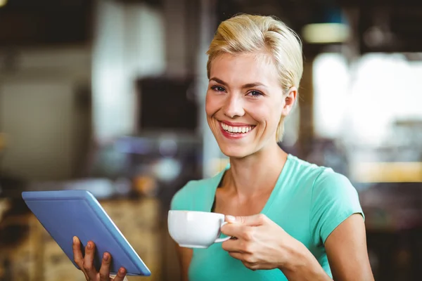 Söt blondin med en kopp kaffe med hjälp av TabletPC — Stockfoto