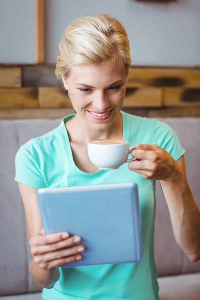 Hübsche Blondine hält Tasse Kaffee und benutzt Tablet-Computer — Stockfoto