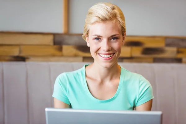 Loira bonita feliz usando o computador e olhando para a câmera — Fotografia de Stock