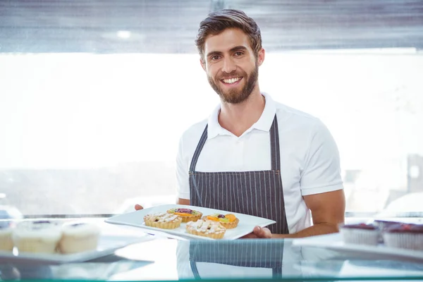 Trabalhador sorrindo segurando pastelaria atrás do balcão — Fotografia de Stock