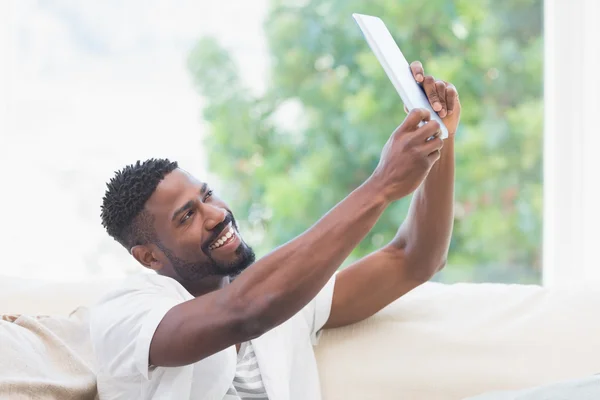 Homem usando comprimido no sofá para tomar selfie — Fotografia de Stock