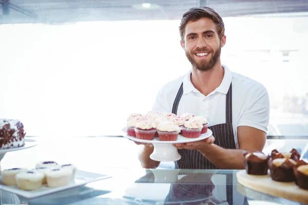 Trabalhador sorrindo segurando cupcakes atrás do balcão — Fotografia de Stock