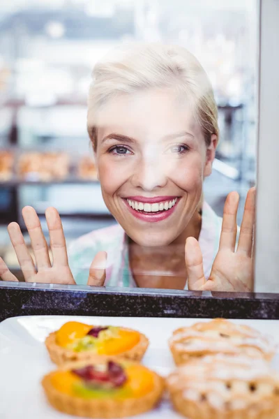 Smiling pretty woman looking at a fruit pie through the glass — Stock Photo, Image