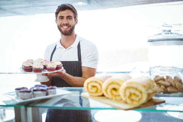 Gülümseyen işçi tezgahın arkasındaki cupcakes holding — Stok fotoğraf