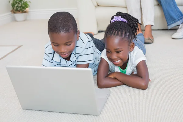 Irmãos felizes deitados no chão usando laptop — Fotografia de Stock