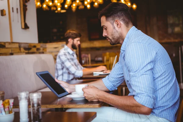 Businessman using tablet while holding cup of coffee — Stock Photo, Image