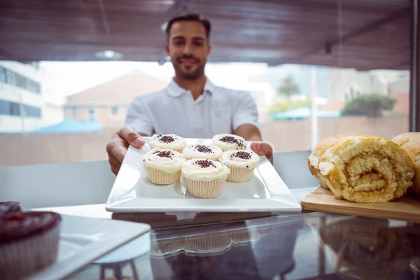 Trabajador sonriente sosteniendo cupcakes detrás del mostrador —  Fotos de Stock