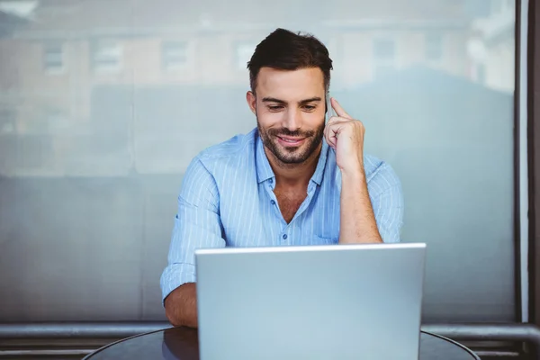 Empresário sorridente no telefone trabalhando no laptop — Fotografia de Stock