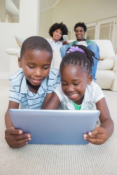 Irmãos felizes deitados no chão usando tablet — Fotografia de Stock