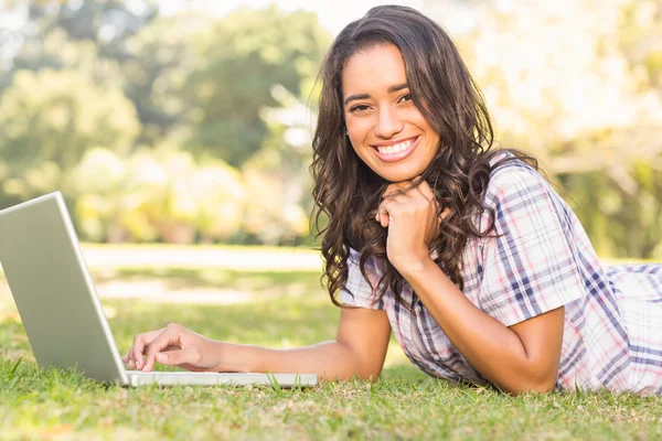 Bruna sdraiata sull'erba e usando il computer portatile — Foto Stock