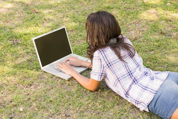 Bruna sdraiata sull'erba e usando il computer portatile — Foto Stock