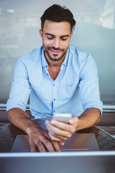 Smiling businessman using phone while working on laptop — Stock Photo, Image