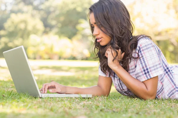 Brunette liggend in gras en met behulp van laptop — Stockfoto