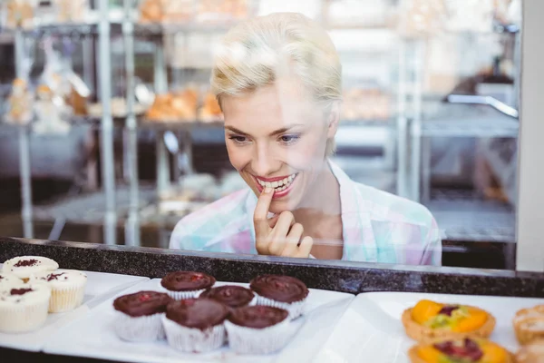 Hesitating pretty woman looking at cup cakes — Stock Photo, Image