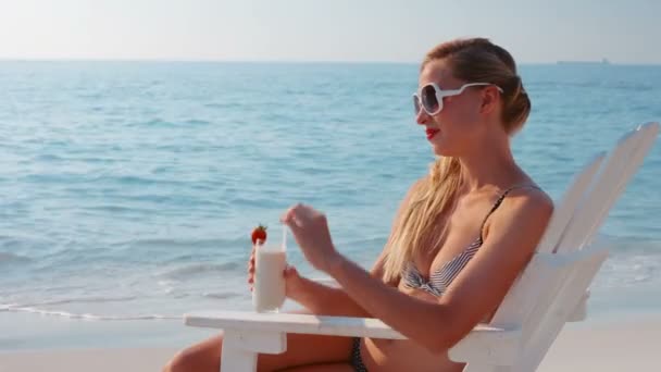 Блондинка пьет коктейль на пляже — стоковое видео
