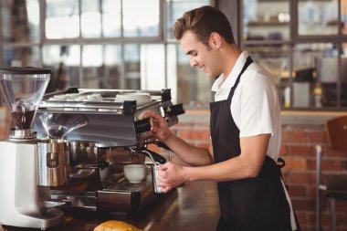 Smiling barista steaming milk at coffee machine clipart