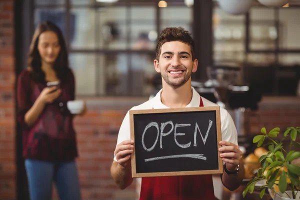 Garçom sorrindo posando com um quadro-negro sinal aberto — Fotografia de Stock