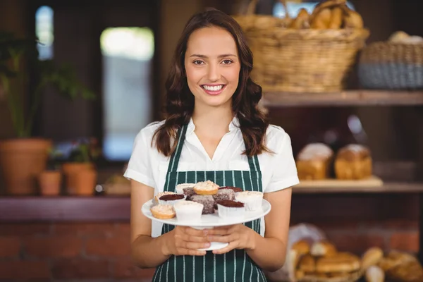 Bastante camarera mostrando un plato de magdalenas — Foto de Stock