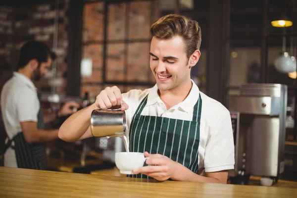 Sorridente barista versando il latte in una tazza — Foto Stock