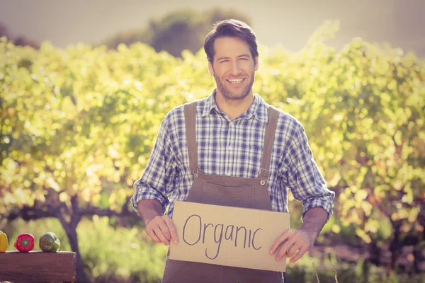 Agricultor sonriente sosteniendo un signo orgánico — Foto de Stock