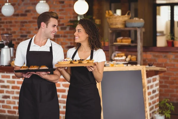 Garçom sorridente e garçonete segurando bandeja com muffins — Fotografia de Stock